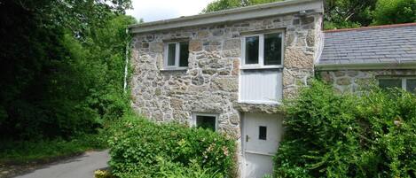 A stone house with a single door and window, surrounded by lush greenery.