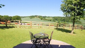 Eine Terrasse mit Tisch und Stühlen mit Blick auf eine umzäunte Weide mit Kühen.