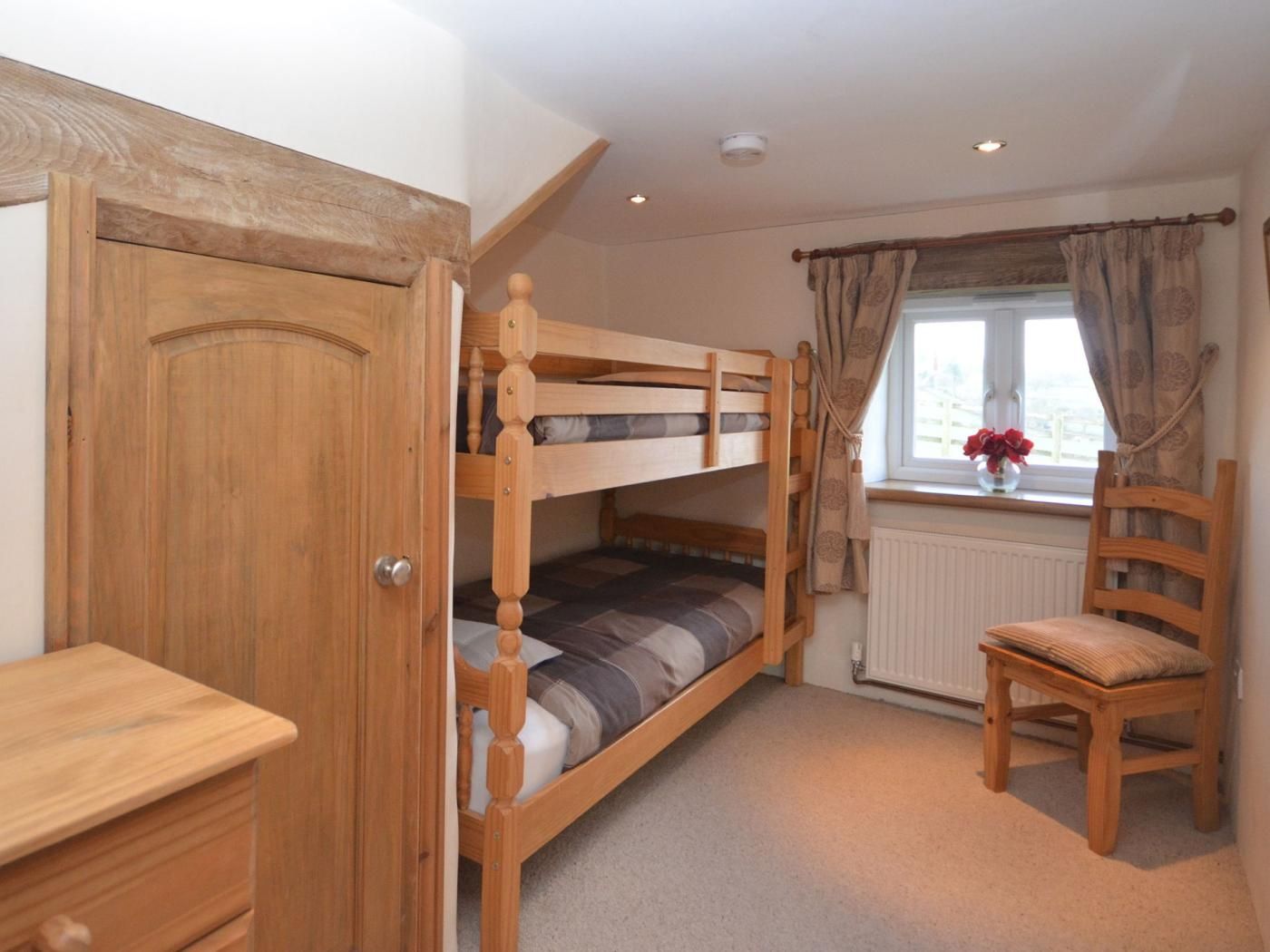 A bedroom with a bunk bed, a wooden chair, a desk, and a window with curtains.