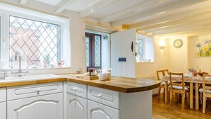 A kitchen with white cabinetry, a wooden countertop, and a dining area with a table and chairs. - 4 Bed in Yelverton (oc-rtide) (Bere Ferrers)