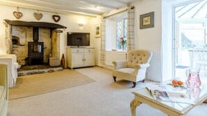 A cozy living room with a stone fireplace, a television, a comfortable armchair, and a dining table with a glass top. - 4 Bed in Yelverton (oc-rtide) (Bere Ferrers)