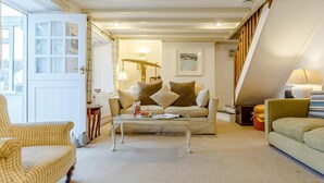 A cozy living room with a sofa, armchair, and coffee table, a staircase, and a window with curtains. - 4 Bed in Yelverton (oc-rtide) (Bere Ferrers)