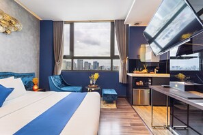 Habitació d'hotel amb un llit gran, escriptori, televisió, vista a la ciutat i petita cuina.