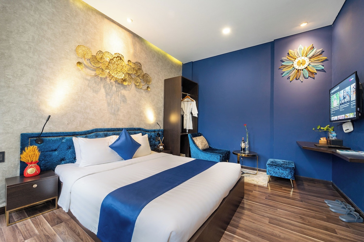Ein modernes Hotelzimmer mit einem großen Bett, einer blauen Akzentwand, einer Wanddekoration, einem Fernseher und einer kleinen Sitzecke.