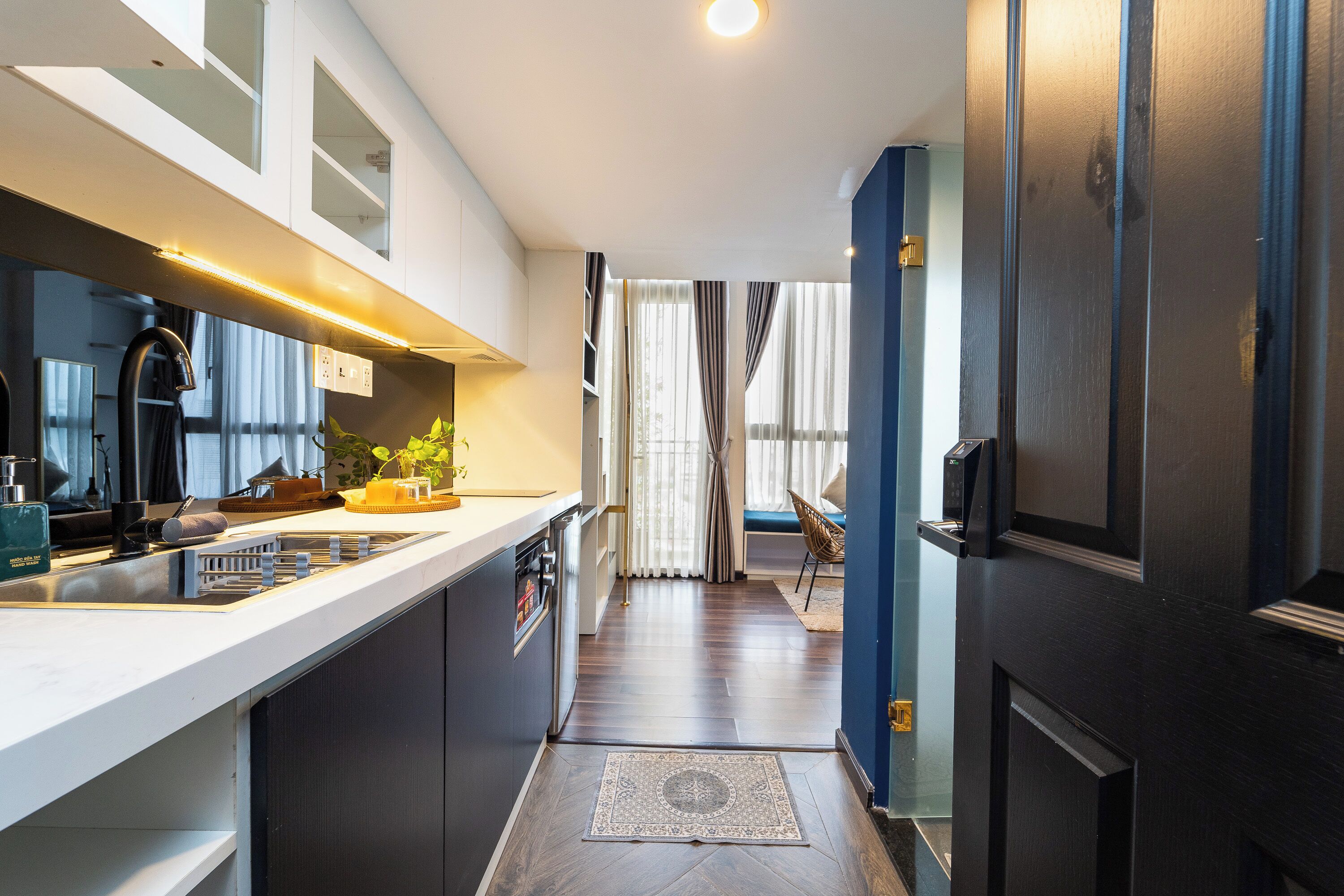 A modern kitchen with a central island, a dining area with a chair, and a view through a doorway.