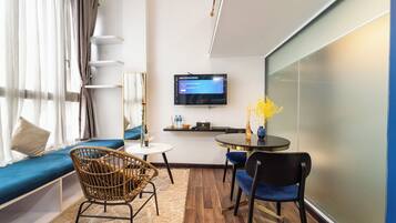 A modern hotel room with a sofa, two chairs, a small table, a TV, and a glass wall.