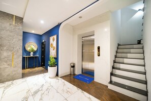 Een moderne lobby met een marmeren vloer, een blauwe wand, een receptiebalie, een welkomstmat, een lift en een trap.
