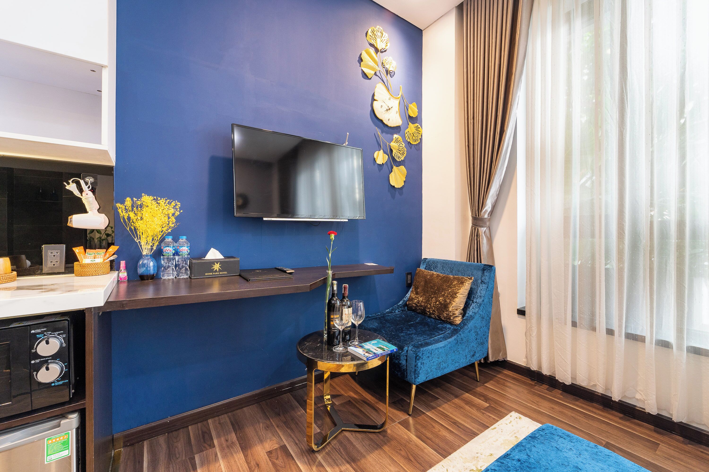 A modern living room with a blue accent wall, a flat-screen TV mounted above a small table, a blue sofa, and a wooden floor.