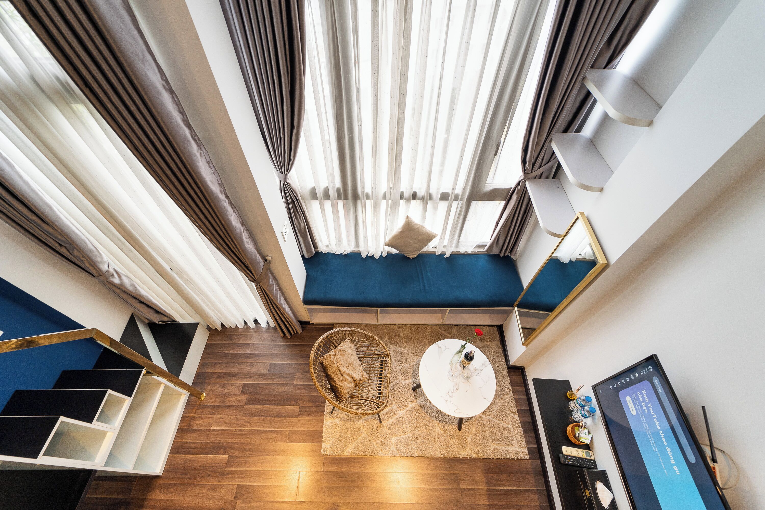 Une pièce moderne avec un canapé bleu, une table basse ronde, un fauteuil en osier et un escalier à marches noires et blanches.