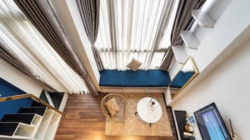 Une pièce moderne avec un canapé bleu, une table basse ronde, un fauteuil en osier et un escalier à marches noires et blanches.