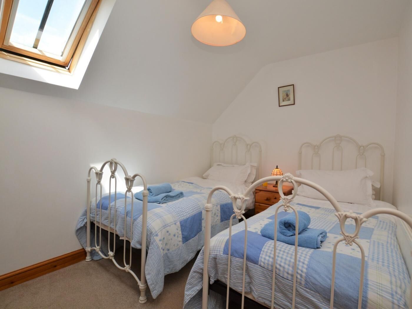 Une chambre avec deux lits, un puits de lumière et une table de chevet avec une lampe.