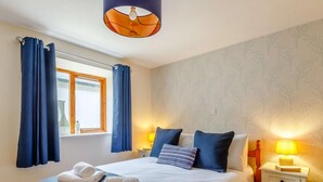 Ein Schlafzimmer mit einem Bett, zwei Nachttischen, einem Vorhangfenster und einer Wand mit Blumenmuster.