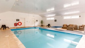 Ein Hallenbad mit Glasdecke, gefliestem Boden und einer Sitzecke mit Korbmöbeln.