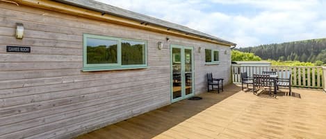 Un bâtiment en bois avec une enseigne indiquant « SALLE DE JEUX », une terrasse avec des meubles d’extérieur et une vue panoramique.