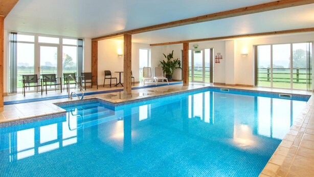 An indoor swimming pool with clear glass walls, wooden beams, and a view of the outdoors. - 3 Bed in Sherborne (oc-folwr) (Folke)