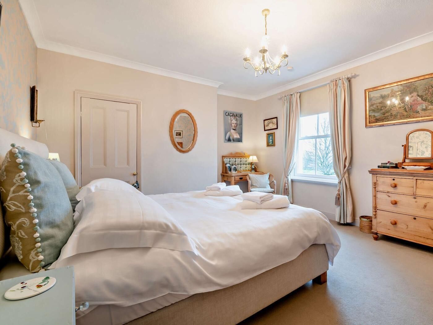 A bedroom with a bed, dresser, and a chandelier.