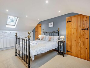 Une chambre à coucher avec un lit, une table de chevet, une armoire en bois, un puits de lumière et un radiateur blanc.