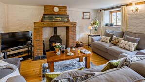 A cozy living room with a brick fireplace, a television, a sofa, and a coffee table. - 3 Bed in Beaworthy (oc-wvfco) (Ashwater)