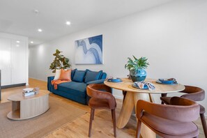 A modern living room with a sofa, coffee table, and dining area with chairs and a table. - Fortitude Valley Hideaway | 6 Guests, 2 Car Bays (Fortitude Valley)