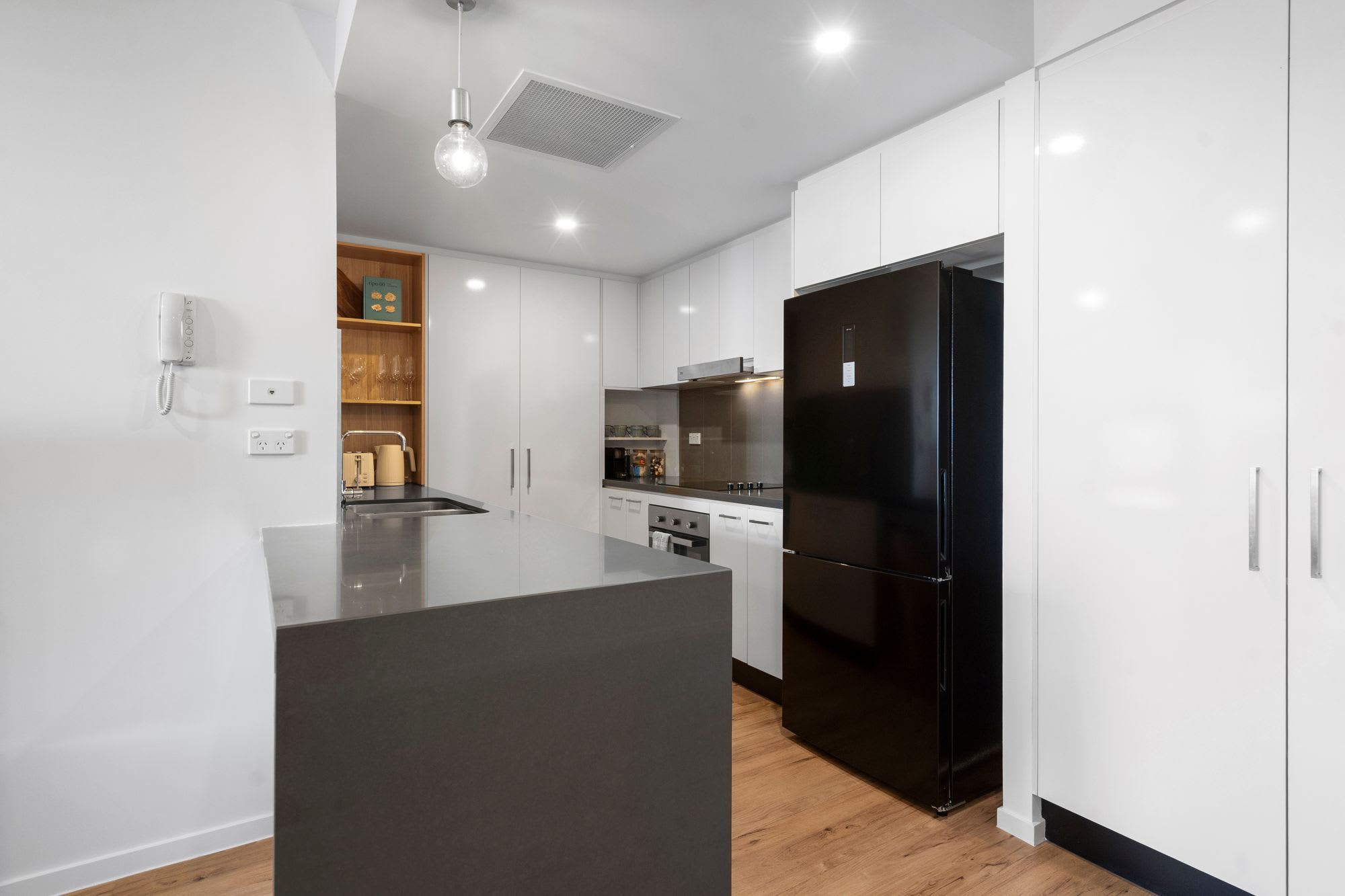 A modern kitchen with white cabinets, a black refrigerator, and a wooden island.
