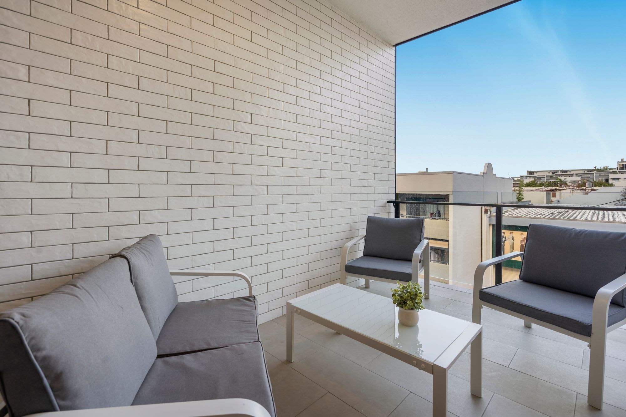 A balcony with a white brick wall, two grey sofas, a small white table, and a potted plant.
