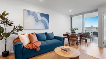 A modern living room with a blue sofa, a round coffee table, and a dining area with chairs.