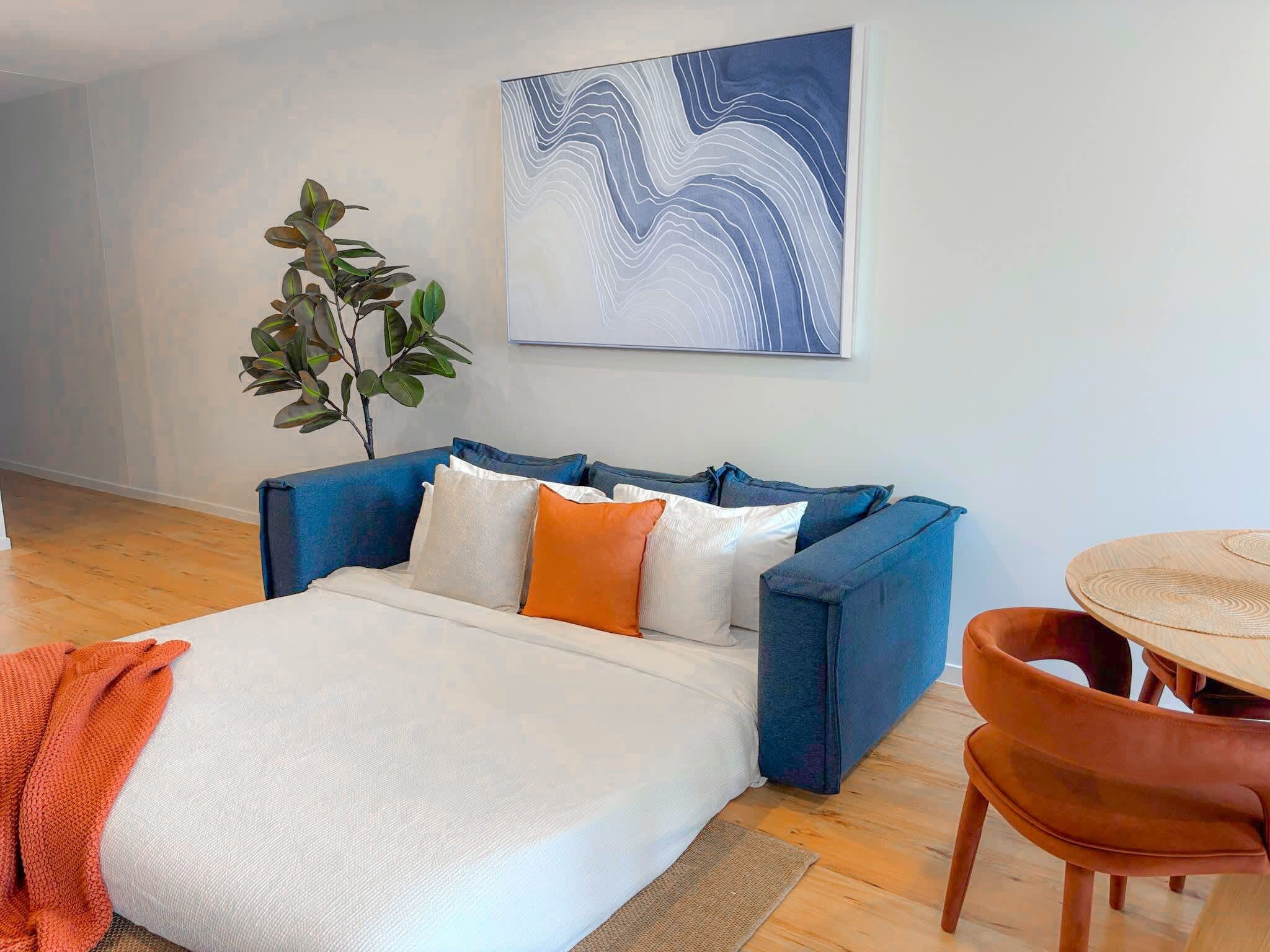 A modern living room with a sofa, a dining table, and a large abstract painting on the wall.