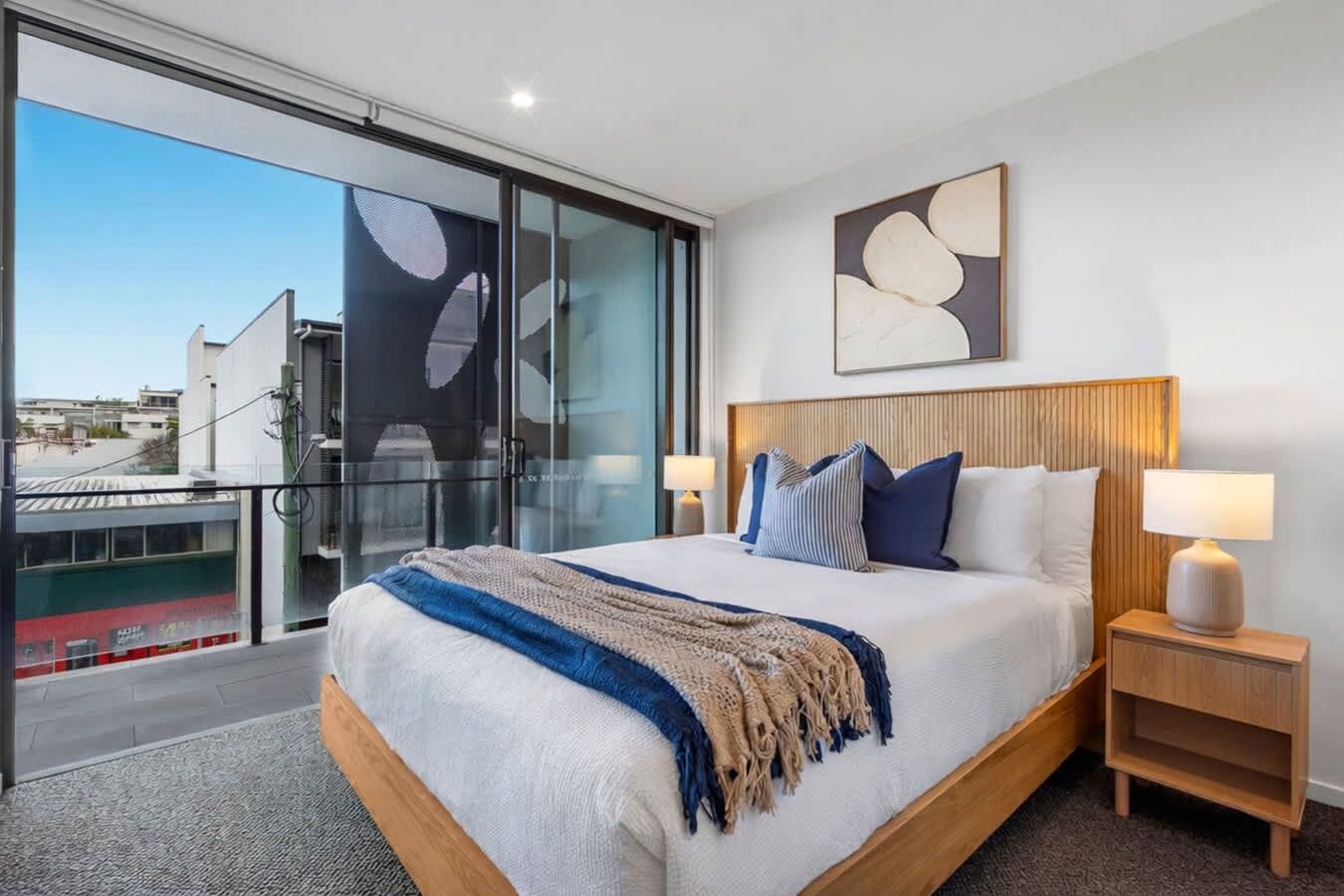 A modern hotel room with a large bed, a view through a glass door, and a cityscape outside.