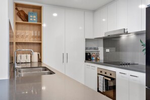 Een moderne keuken met witte kastjes, roestvrijstalen apparatuur en een houten plank met keukengerei.