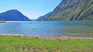 A lake with mountains in the background, a grassy shoreline, and a few people in the water. - Casa Gloria by Interhome (Porlezza)