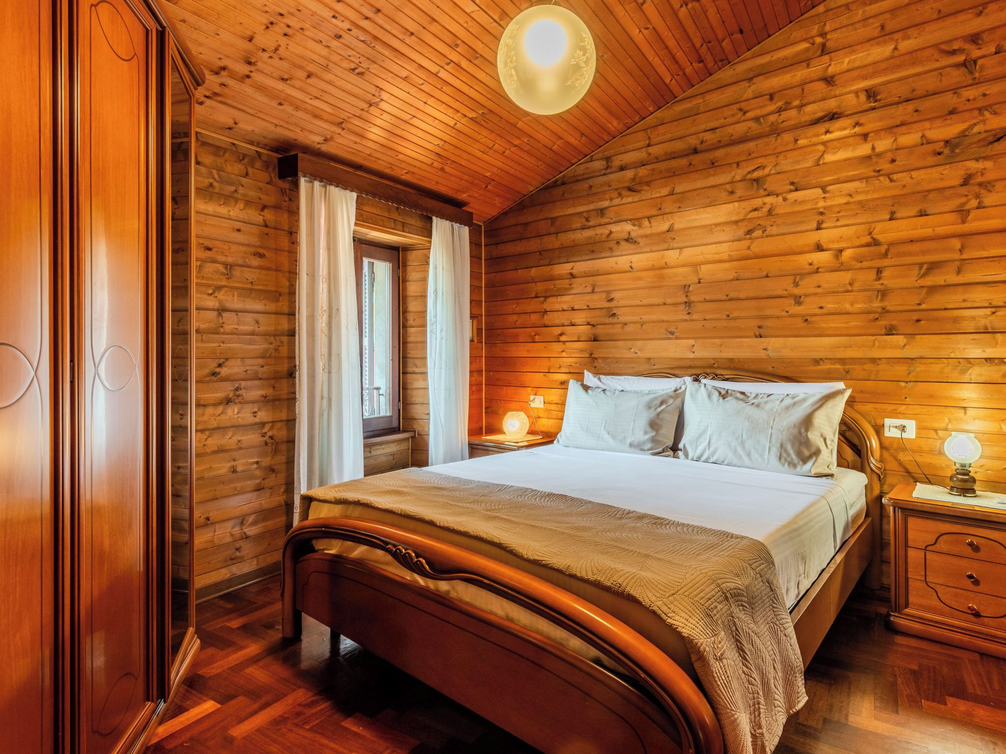 A wooden-paneled bedroom with a bed, nightstands, and a window with curtains.