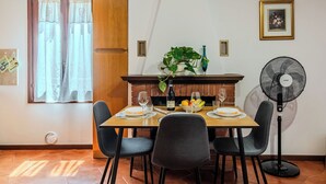 A dining area with a wooden table set for two, surrounded by chairs, a brick fireplace, and a wall-mounted fan. - Casa Gloria by Interhome (Porlezza)
