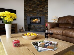 A living room with a fireplace, a leather sofa, a vase with yellow flowers, a candle, a basket of fruit, and magazines on a coffee table. - 4 Bed in Rosedale Abbey (oc-g0074) (Rosedale West Side)
