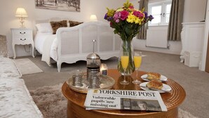 Ett hotellrum med en säng, ett nattduksbord med en lampa, ett soffbord med en tidning, en vas med blommor och ett fönster.