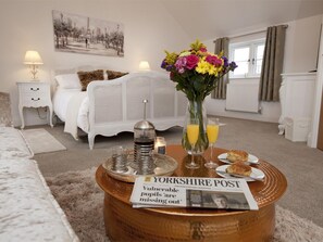A hotel room with a bed, a bedside table with a lamp, a coffee table with a newspaper, a vase with flowers, and a window. - 4 Bed in Rosedale Abbey (oc-g0074) (Rosedale West Side)