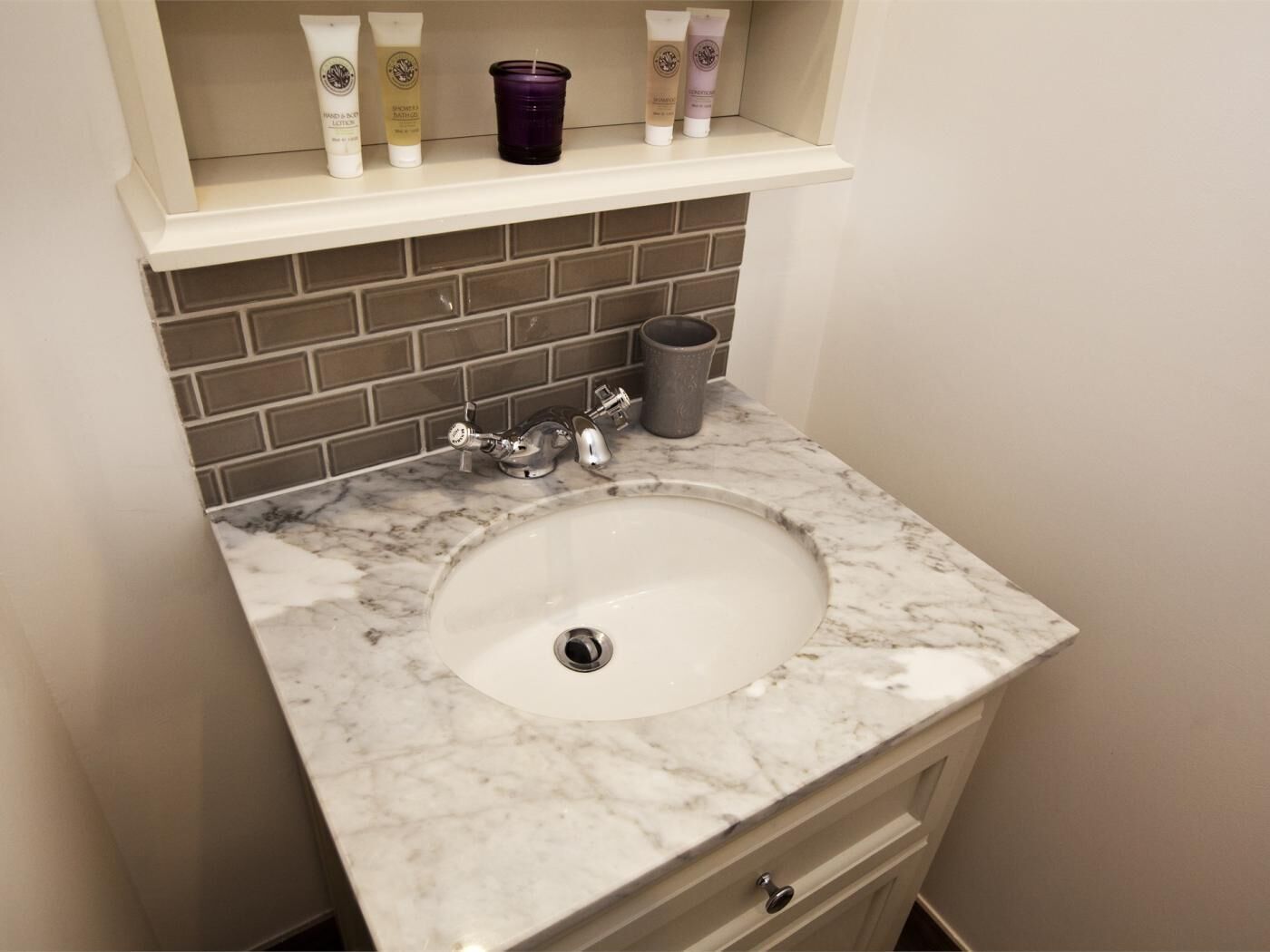 Un baño con lavamanos de mármol, grifo, repisa con artículos de aseo y salpicadero de azulejos.