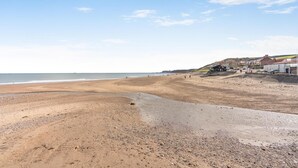 A beach with a pebble beach, a promenade, and buildings in the background. - 2 Bed in Sandsend (oc-g0128) (Sandsend)