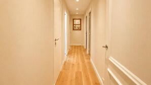 Un couloir doté d’un plancher en bois, de murs blancs et de portes de part et d’autre.