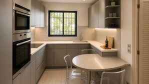 Una cocina moderna con electrodomésticos integrados, una ventana y un comedor con sillas transparentes.