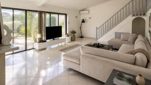 Amplia sala de estar con un ventanal, televisor de pantalla plana, sofá, mesa de centro y escalera.