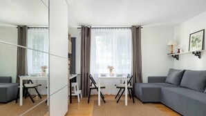 A modern living room with a grey sofa, a dining table with chairs, a small kitchen area, and a large mirror. - Bright Studio in Center | Desk | Close to the Park (Kraków)