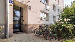 A building entrance with a bicycle parked outside, a sign above the door, and a garden with flowers. - Bright Studio in Center | Desk | Close to the Park (Kraków)