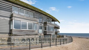 Ein Küstengebäude mit Balkon, Steinunterbau und Blick auf den Strand.