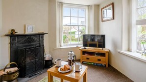 Ein gemütliches Wohnzimmer mit Kamin, Fernseher und einem Fenster mit Blick ins Freie.