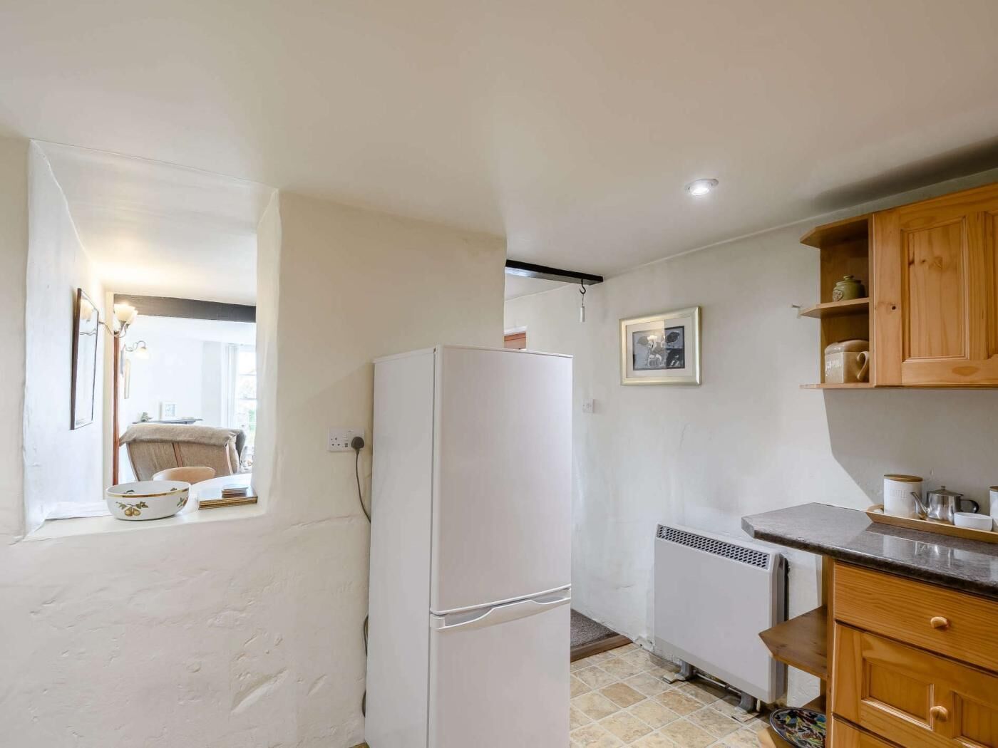 A compact kitchen with a refrigerator, wooden cabinets, a countertop, and a window with a chair outside.