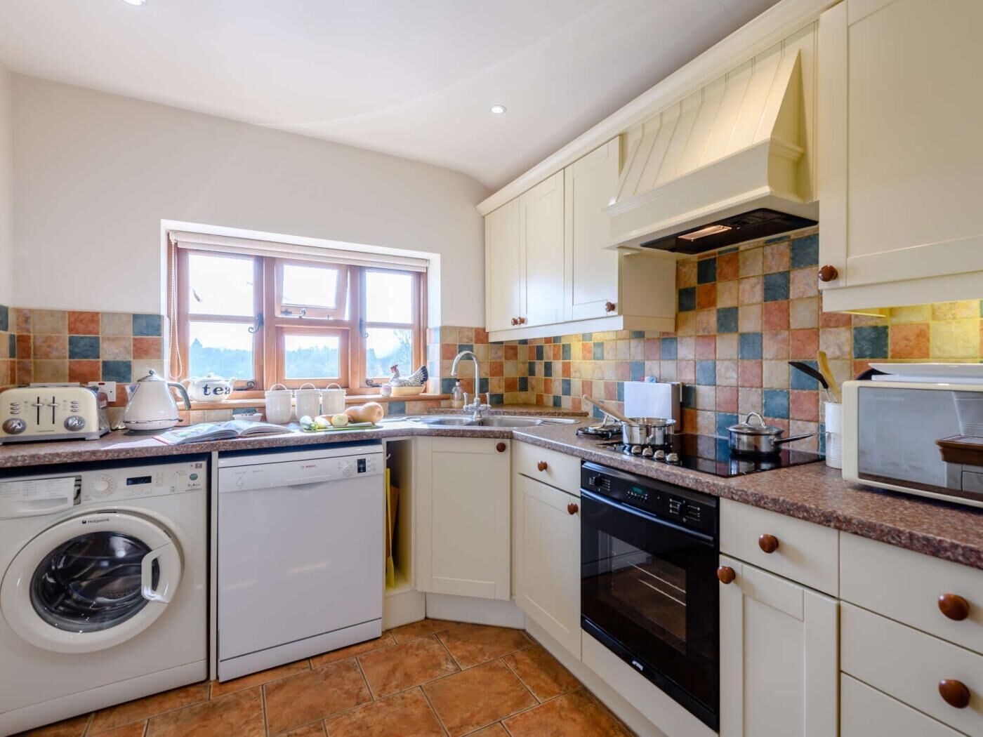 A compact kitchen with a washing machine, oven, and a window with a view.