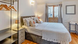 Een slaapkamer met een bed, nachtkastje, lamp, kledingkast en een raam met gordijnen.