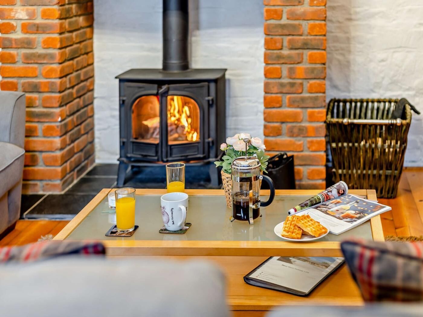 A cozy room with a brick fireplace, a coffee table with breakfast items, and a wicker basket.