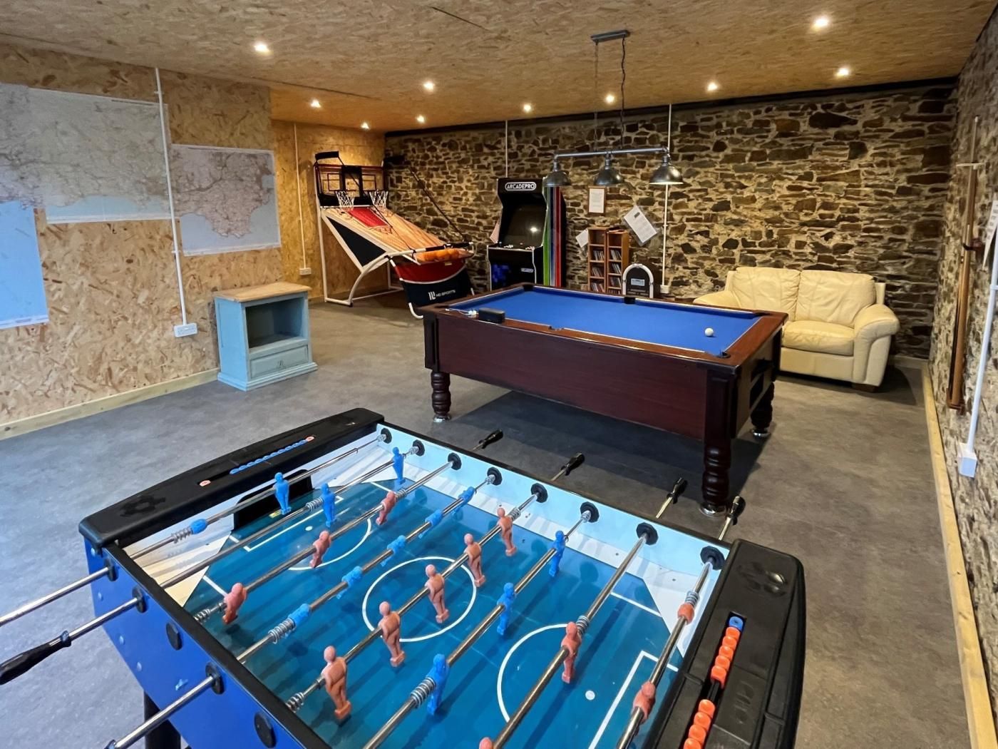 A room with a foosball table, a pool table, a sofa, and a stone wall.