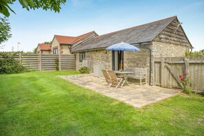A stone building with a sloped roof, a patio with a table and chairs, and a wooden fence. - 2 Bed in Weymouth (oc-swals) (Chickerell)